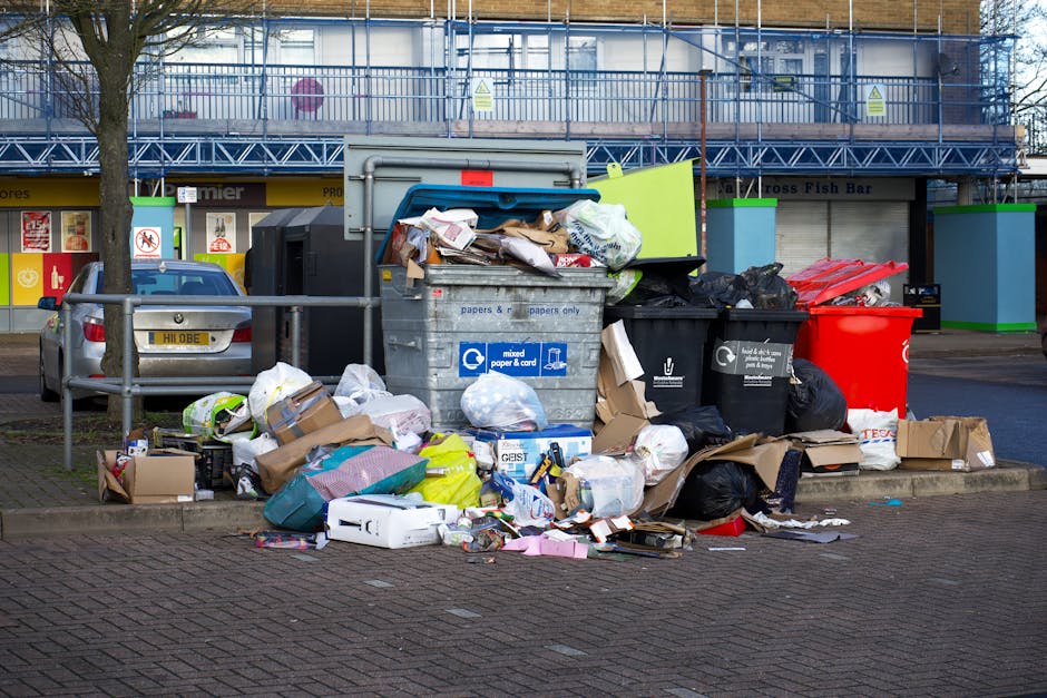 A large pile of black plastic rubbish bags filled with waste is stacked against a tiled wall outdoors. Several clear plastic bottles are visible protruding from the bags, indicating bottle recyclables